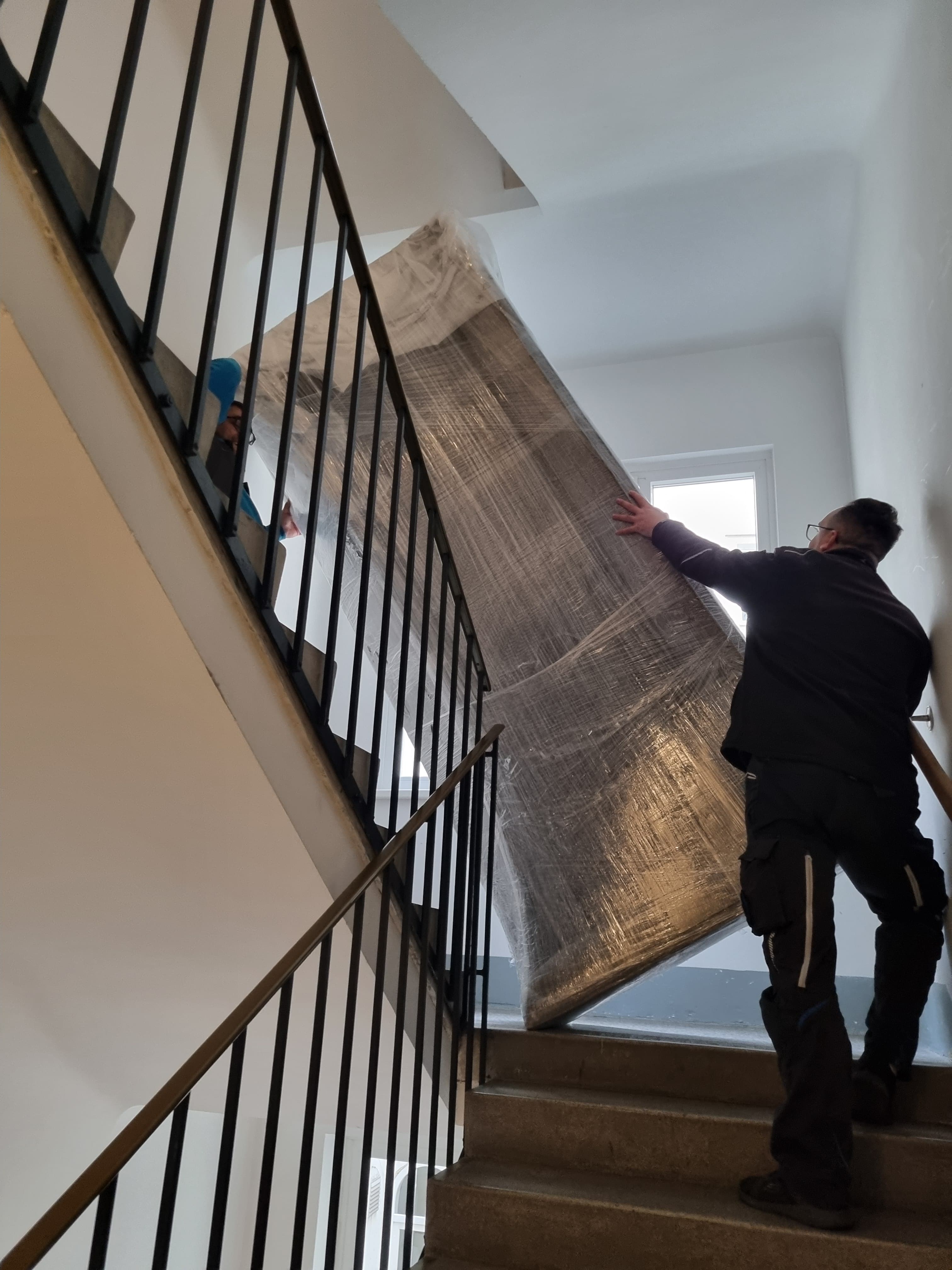 Mitarbeiter tragen ein großes Sofa vorsichtig durch ein enges Stiegenhaus