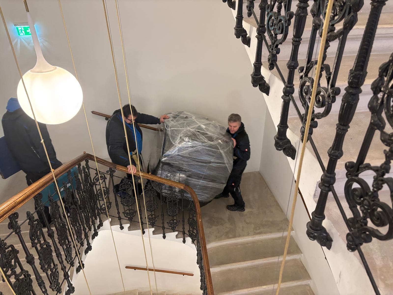 Das A-Team bewegt eine sorgfältig verpackte Wiener Würfeluhr durch ein kunstvoll gearbeitetes Stiegenhaus